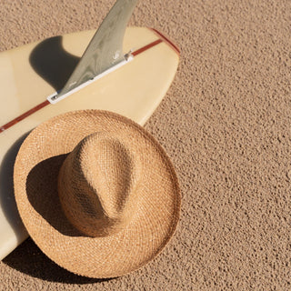 Straw beach hat lying in full sun with surfboard