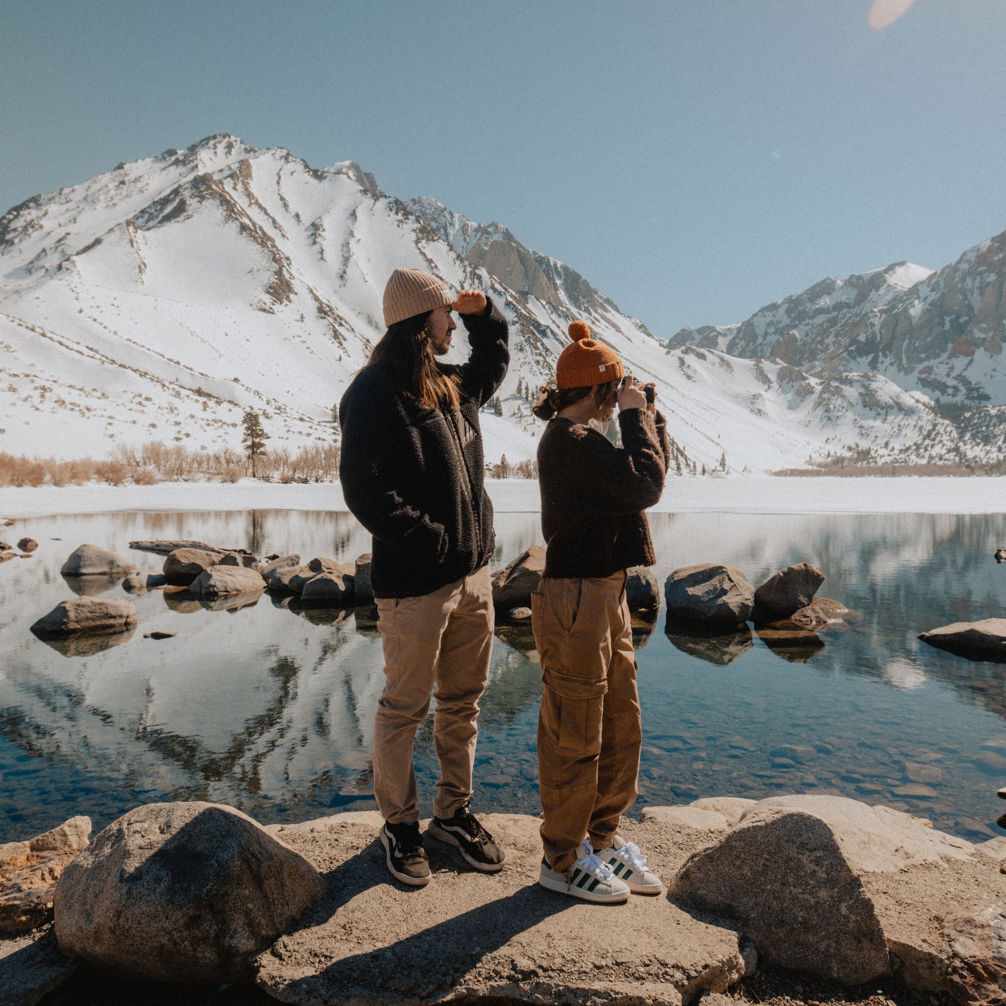 A man and a woman wearing beanies and taking photos at Convict Lake, California