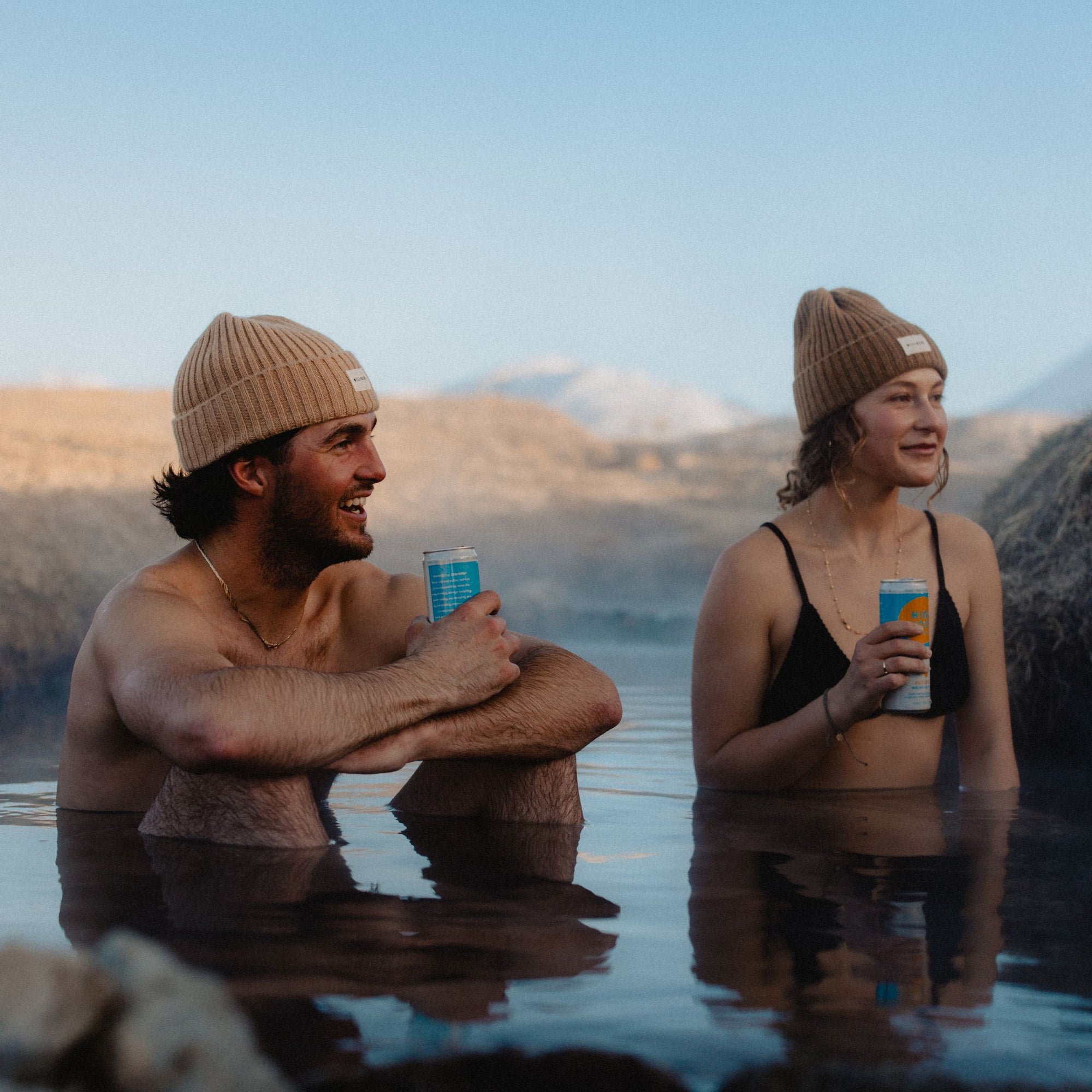 Man and woman wearing beanies and sitting in hot spring