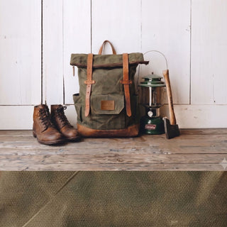 Green backpack, brown boots, camping stove, and axe on a wooden surface with white wooden wall background