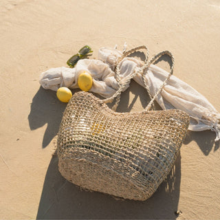 Woven bag with lemons and sunglasses on a sandy surface