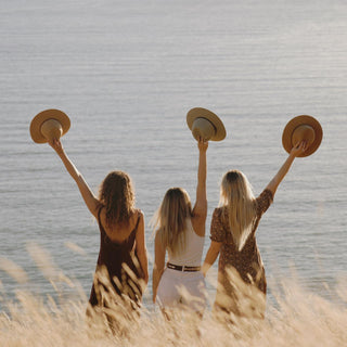 women holding floppy wide-brim hats in the air