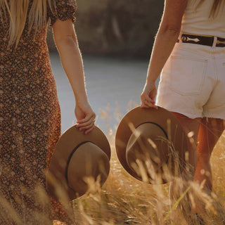 Two women holding floppy wide-brim hats