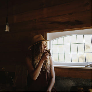 Woman drinking cup of tea wearing a floppy widebrim hat