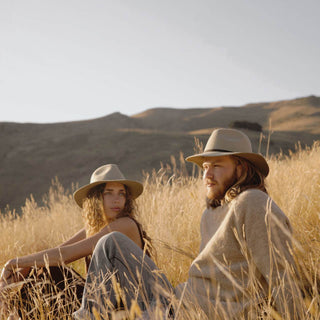 Man and woman sitting in the field wearing wide-brim floppy hats