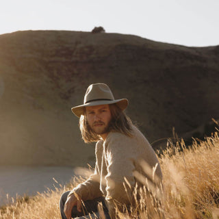 Man sitting in field wearing wide brim floppy hat