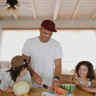 Dad and kids cutting up fruit while wearing the Archie Maroon 5 panel cap