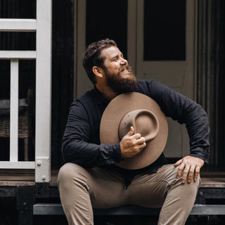 Man holding Australian Outback Explorer hat taupe brown sitting on stairs