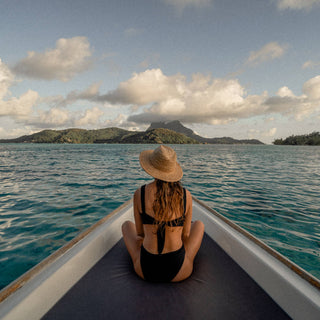 A woman with long blonde hair wearing a straw wide brim hat, sitting in a boat.