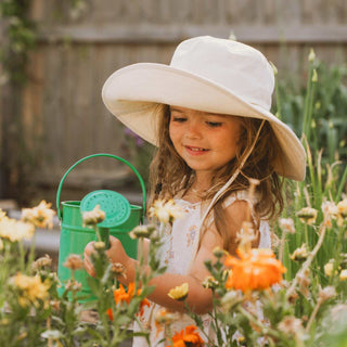 Little girl wearing kids white cream bucket hat Little Bodhi Bone while watering the garden