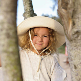 Girl sitting a tree wearing a white cream bucket hat