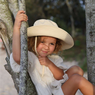 Girl sitting a tree wearing a kids white cream bucket hat with strap