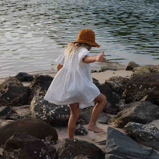 Little girl at the beach wearing orange bucket hat Little Lenny rust