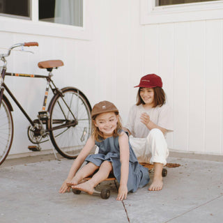 Siblings sitting on a skateboard wearing the archie maroon kids hat