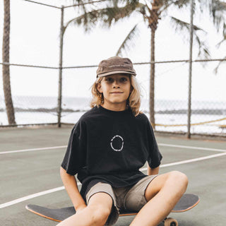 Kid sitting on a skateboard by the ocean wearing Little Archie Walnut kids hat