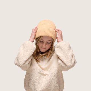 Girl wearing Little Bambi Apricot orange knit beanie while holding her head