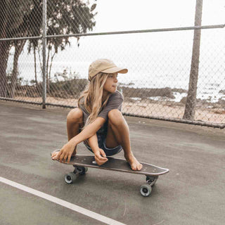 Girl riding skateboard wearing Little Riley Bone kids hat