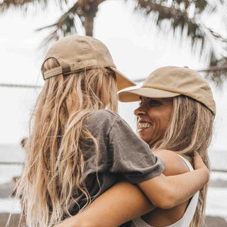 Woman and girl hugging while wearing Riley Gold baseball cap and Little Riley Gold kids hat