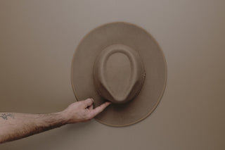 Top down of a hand pointing to the front of a brown Will & Bear hat