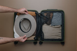 Will & Bear hat being placed in-between clothes in a carry on suitcase