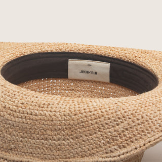 Close-up of a woven hat with a visible brand label on a neutral background