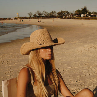 A woman wearing a raffia straw hat on a beach with a scenic background
