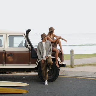 Man & woman sitting on a vehicle wearing a string bucket hat