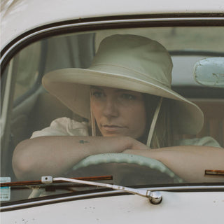 Woman driving a car while wearing bodhi bone white cream bucket hat