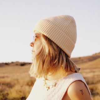 Woman wearing the Will & Bear Bambi Apricot merino wool beanie, standing side-on in a golden field at sunset.