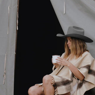 Woman wearing the Will & Bear Buck Smoke black felt cowboy hat at a campsite, captured beside a canvas tent with a mug in hand.