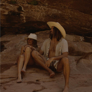 Relaxed couple wearing the Will & Bear Calloway Bone white straw felt fedora in a shaded rocky canyon.