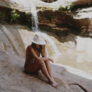 Woman wearing the Will & Bear Calloway Bone white straw felt fedora while seated by a natural waterfall.