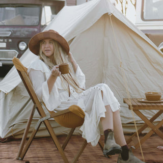 Woman relaxing in the Will & Bear Camp Bodhi Carob recycled hemp bucket hat outside a canvas tent during golden hour.