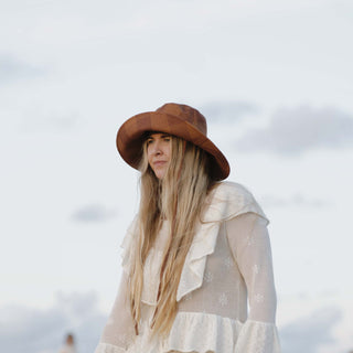 Woman standing in a breezy white dress and the Will & Bear Camp Bodhi Carob recycled hemp bucket hat under open skies.