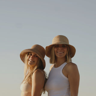 Two women at the beach wearing Will & Bear Crushable Straw Bucket Hats, perfect for sun-filled adventures