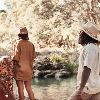 Couple beside a creek, both wearing wide brim hats styled with the Will & Bear Hat Scarf Mustard as a bold band feature.