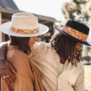 Two people embracing, both wearing hats with the Will & Bear Hat Scarf Mustard tied in different styles.