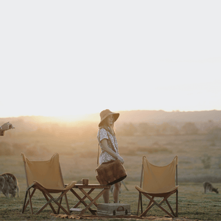 Will & Bear x Wandering Folk Slow Road Camp Chairs in a grassy field at golden hour with a woman walking nearby.