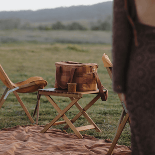 Will & Bear x Wandering Folk Slow Road Camp Table styled with crockery beside a caravan for a rustic outdoor setup.