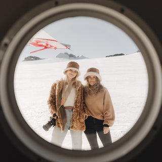 Two women captured through plane window wearing Will & Bear Wool UGG Bucket Hats before snowy expedition