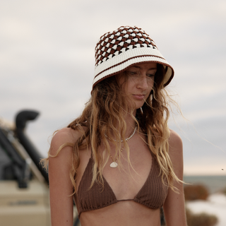 A woman wearing a brown and white patterned hat and a brown bikini top on a beach.