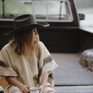 Woman wearing the Will & Bear Buck Smoke black felt cowboy hat while sitting in the tray of a ute, holding a coffee mug.