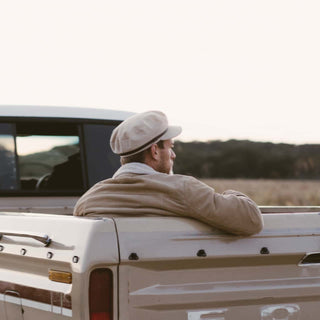 Back view of man sitting on a truck bed wearing Will & Bear Baker Fawn white cord newsboy cap.