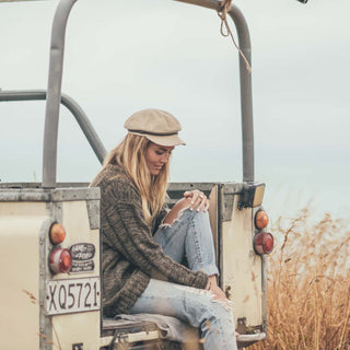 Woman wearing Will & Bear's white cord newsboy cap, Baker Fawn, styled with relaxed outfit beside a truck.