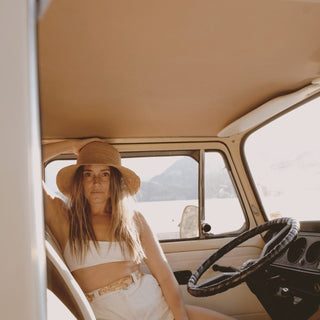 Woman sitting in the driver’s seat of a camper van wearing the Will & Bear Bobby Sand straw bucket hat.