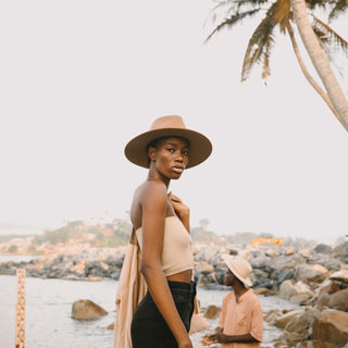 Woman by rocky shoreline wearing Will & Bear Brown Wide Brim Fedora, made for outdoor explorers