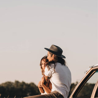 Couple sitting on top of a car, both wearing Will & Bear Calloway Ash wide brim felt fedoras, enjoying sunset views.