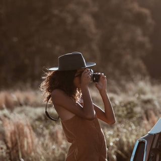 Woman wearing the Will & Bear Calloway Ash wide brim felt fedora while gazing into the distance in a golden field.