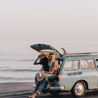 Couple wearing the Will & Bear Calloway Cream white sun felt hat sitting in a vintage van boot by the ocean.