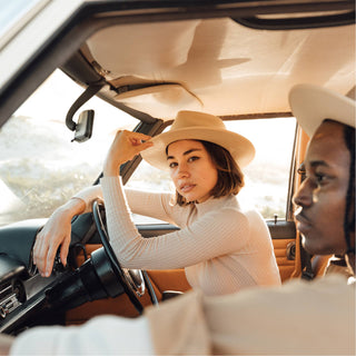 Interior view of woman driving in the Will & Bear Calloway Cream white sun felt hat with sunlight pouring through the van windows.